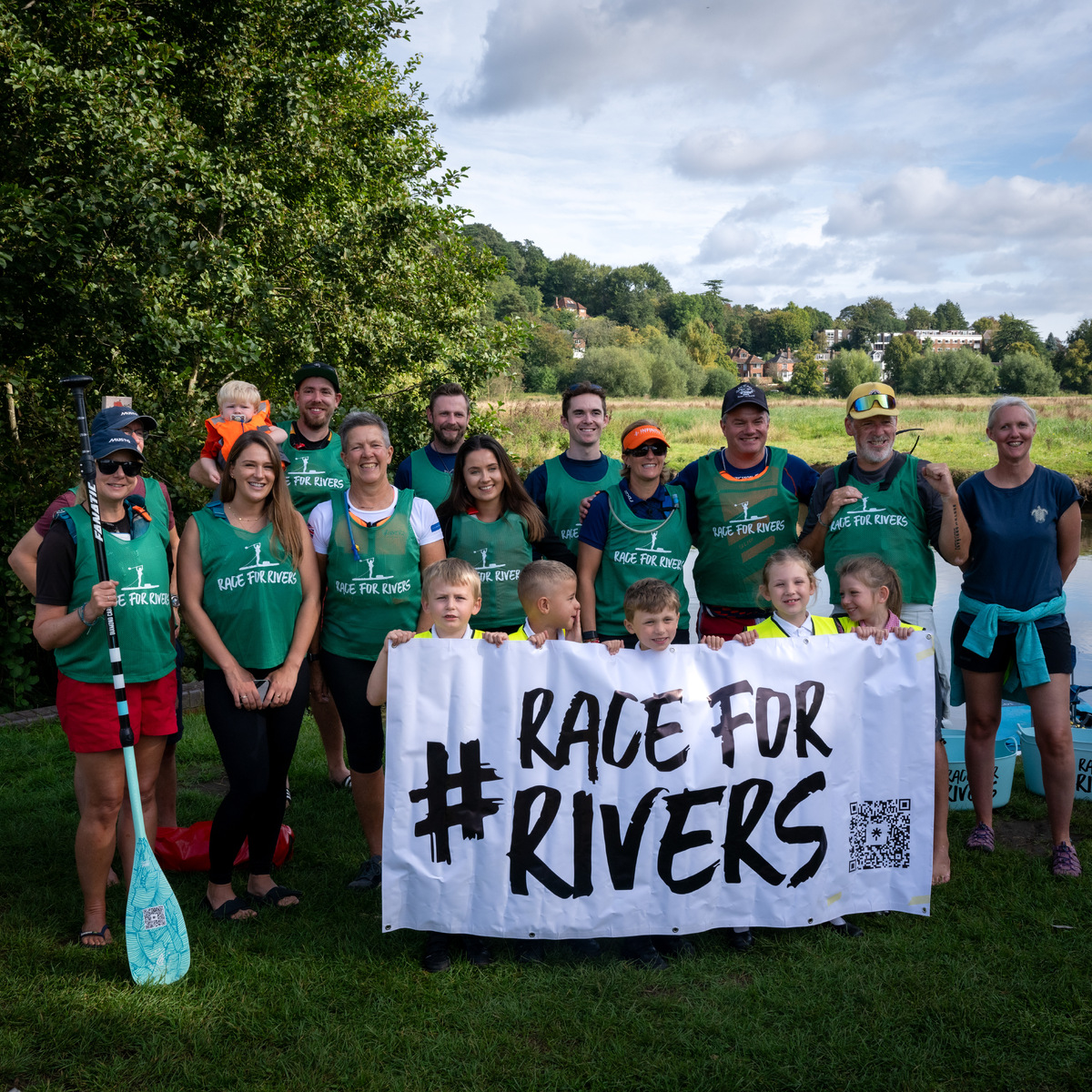 A group of people standing in a field holding a sign that reads #RaceForRivers